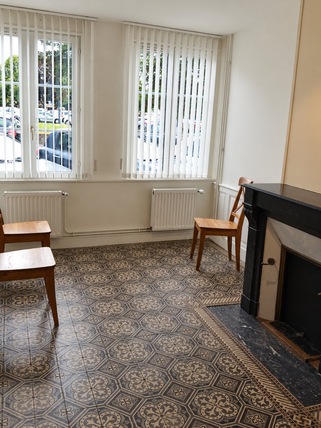 Salle avec carreaux de ciment, cheminée en marbre noir et chaises en bois